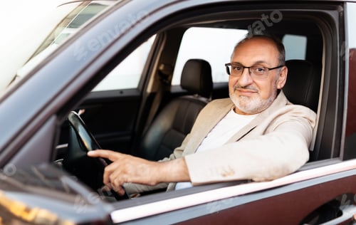 Preview: A man wearing glasses poses confidently in his car during daylight