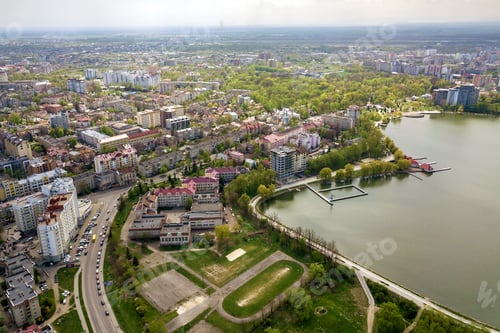 Preview: Aerial view of city lake among green trees and town buildings in recreation park zone.