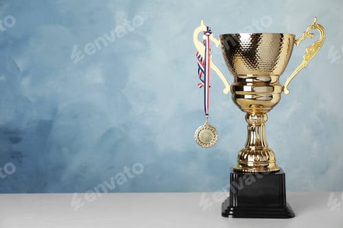Preview: Golden trophy cup and medal on table against blue background. Space for text
