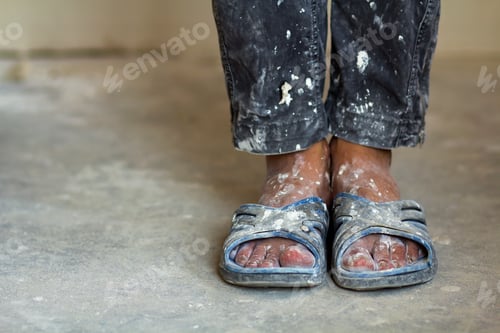 Preview: Feet of a construction worker in old dirty clothes and shoes