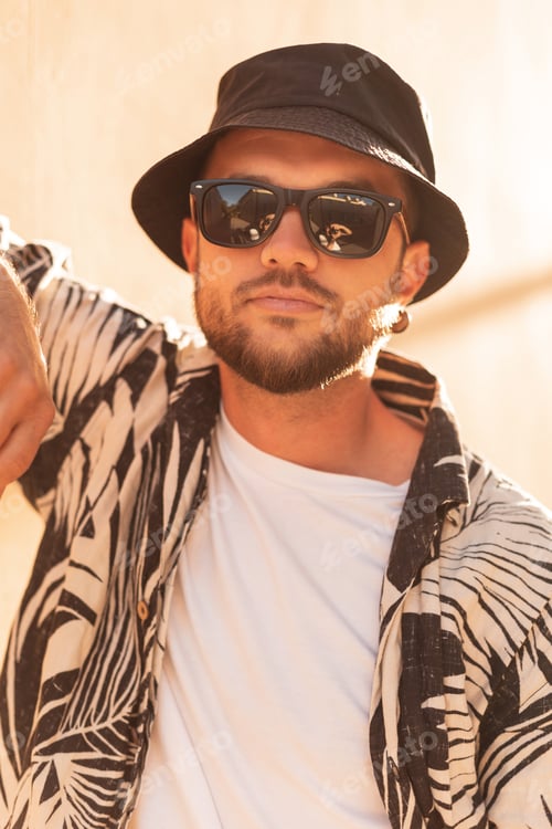 Preview: Hipster man with sunglasses in fashion shirt and hat at sunset