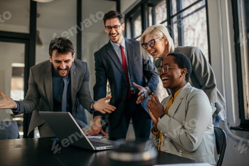 Preview: Business team celebrating success while looking at laptop in office