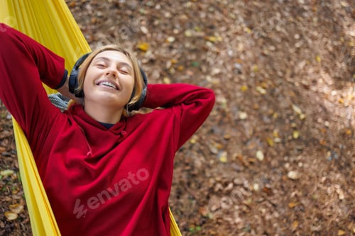 Preview: Girl in headphones is lying on a yellow hammock in the forest