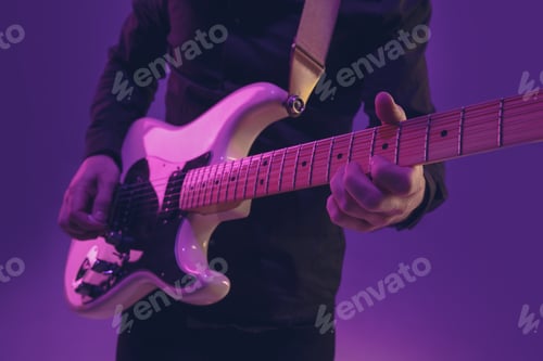 Preview: Young caucasian musician playing guitar in neon light on purple background