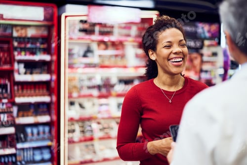 Preview: A smiling African adult woman talking with a male pharmacist in a makeup store.