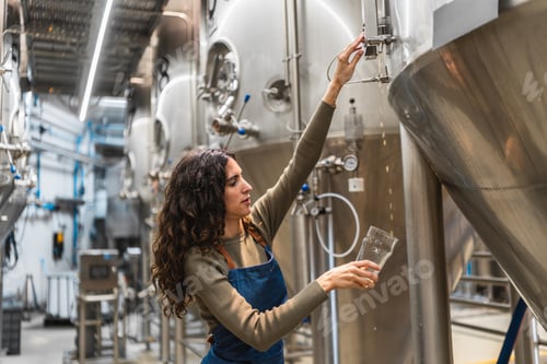 Preview: Woman brewer checking beer quality in brewery producing tanks