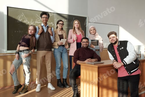 Preview: Group of intercultural cheerful students in casualwear looking at you while standing by teacher