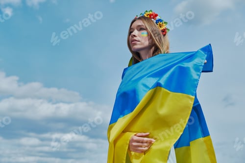 Preview: Confident young Ukrainian woman covering with national flag with sky in the background
