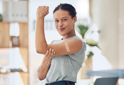 Preview: Young happy mixed race woman showing and holding her arm with a bandaid after getting a vaccine. Be