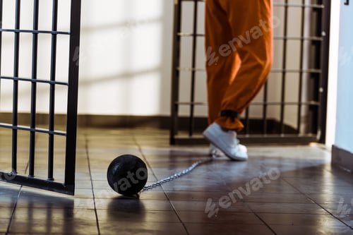Preview: cropped image of prisoner walking in orange uniform with weight tethered to leg