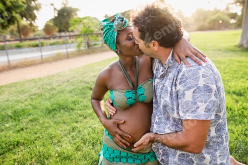 Preview: Happy African pregnant woman having tender moment kissing her husband in park during sunset time
