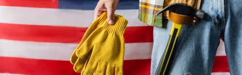 Preview: cropped view of workman with hammer in tool belt holding work gloves near usa flag, labor day