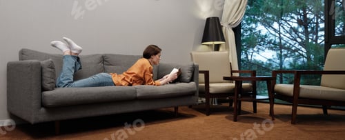 Preview: Young woman relaxing on a cozy sofa, reading a book in a modern living room with a serene view