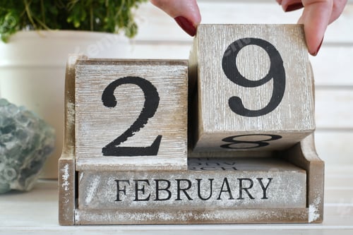Aperçu: Female changing date to Leap Year Day, February 29, displayed on a wooden block calendar - concept
