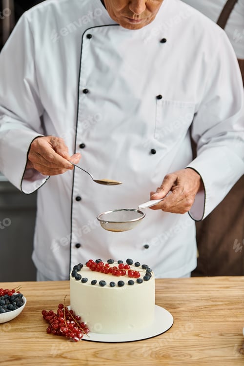 Preview: cropped view of mature chef decorating his delicious sweet cake with brown sugar, cooking courses