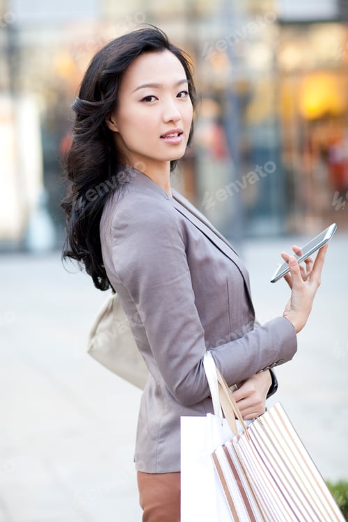 Preview: Happy young woman with shopping bags and smart phone