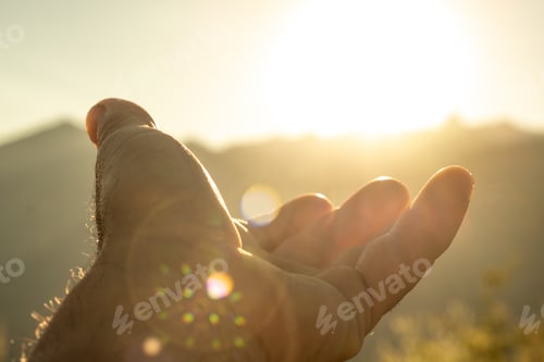 Preview: closeup of a man's hand towards the horizon catching the sun