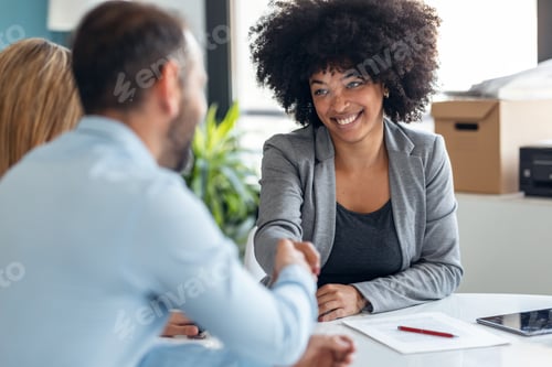 Preview: Attractive real-estate agent shaking hands with young couple after signing agreement contract