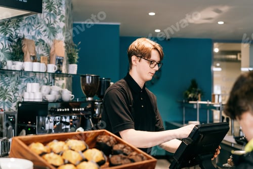 Preview: Young waiter serving customer at cash point in cafe. Man working with POS terminal. Cashier, barista