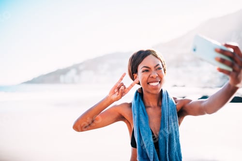 Preview: Afro American young women taking funny selfie with smartphone after workout at beach