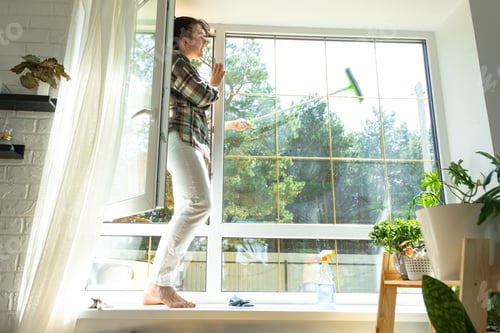 Preview: Woman manually washes the window of the house with a rag with spray cleaner and mop inside the inter