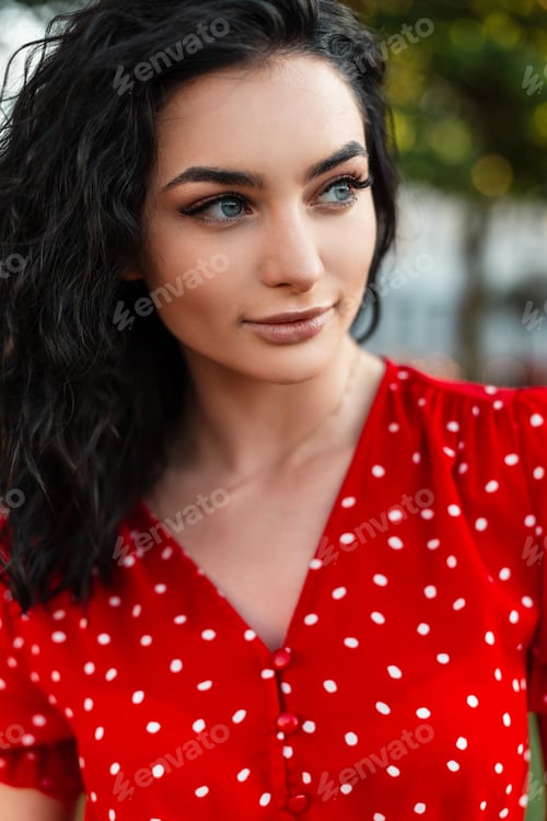 Preview: Beautiful young curly girl with blue eyes and red retro dress in the park