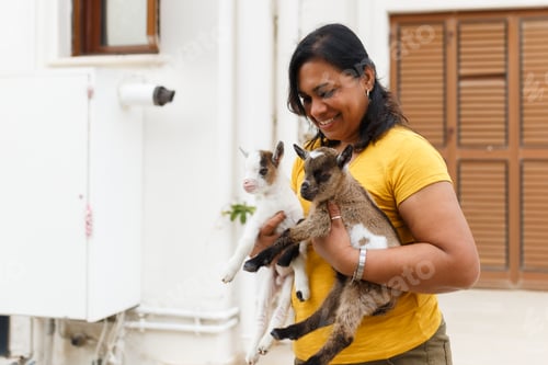 Preview: Woman holding two cute newborn baby goats smiling