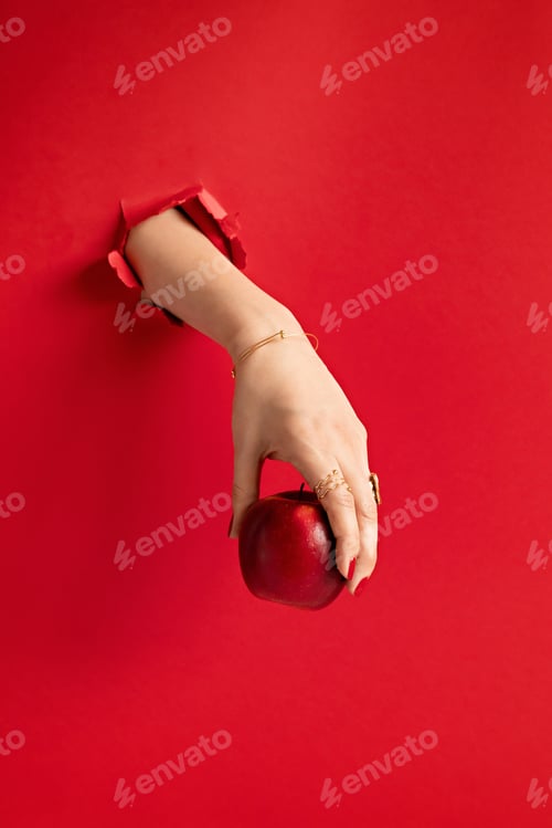 Preview: Woman hand holding red apple through the hole in red paper