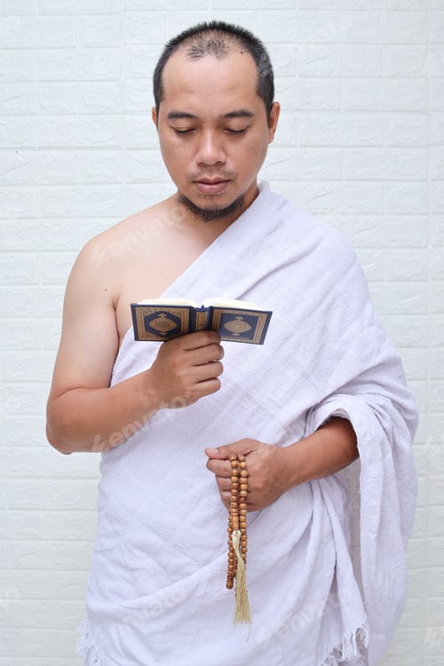 Preview: Muslim man wearing white ihram clothes, reciting quran while holding prayer beads
