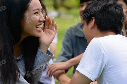 Preview: Two young Asian friends whispering together at the park