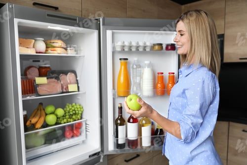 Preview: Woman with apple near refrigerator in kitchen