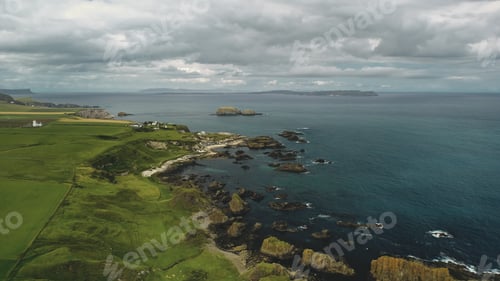 Preview: Rocky shore aerial view: green grass meadows and fields. Water surface stretches to horizon