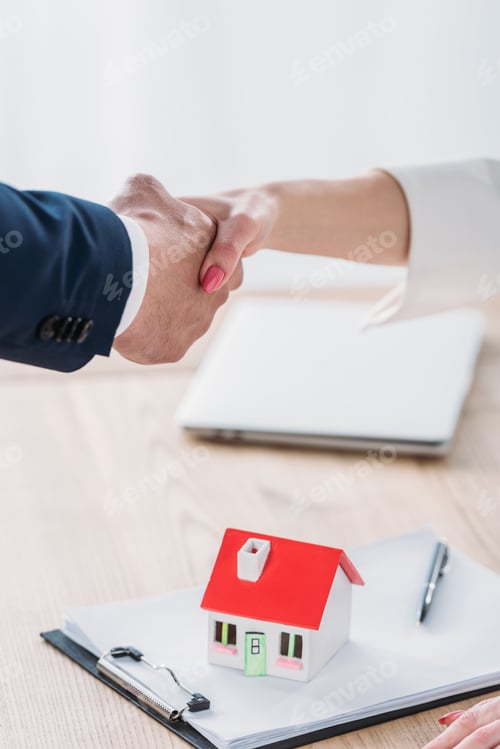 Preview: partial view of businessman shaking hands with client near house model on tabletop