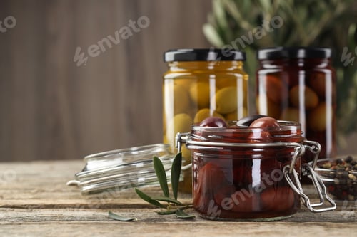 Preview: Pickled olives in glass jars and spices on wooden table, closeup. Space for text