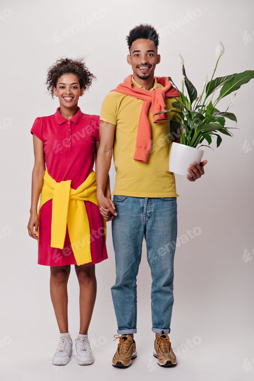 Preview: Charming woman and man holding hands and posing with plant on isolated background. Dark-skinned guy