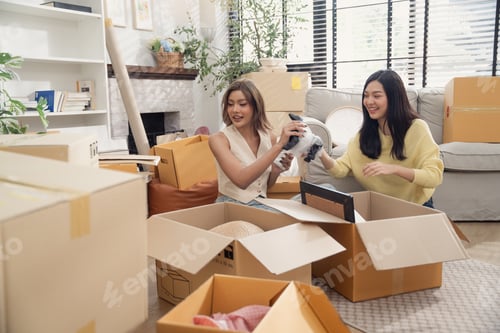 Preview: Asian girl friends unpacking stuff from cardboard boxes at the new house.