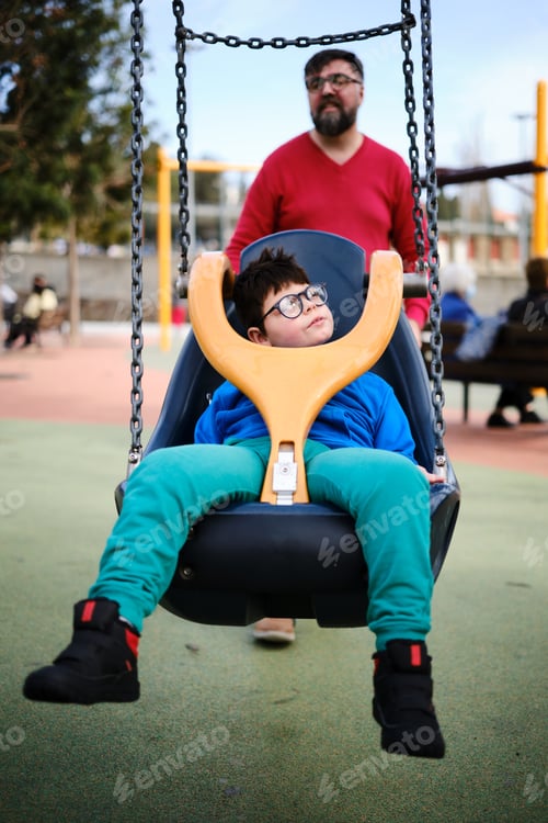 Preview: Disabled boy swinging on a special needs swing while enjoying with his father at the playground.