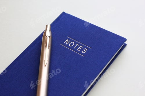 Preview: Flat lay blue notebook and gold pen on a white background