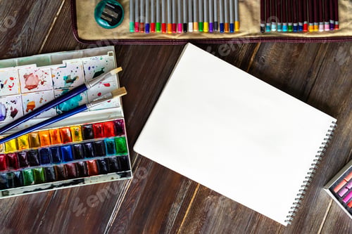 Preview: workplace, pencils, brushes, watercolor paints, paper crayon pastel chalks. Flat lay, wooden table