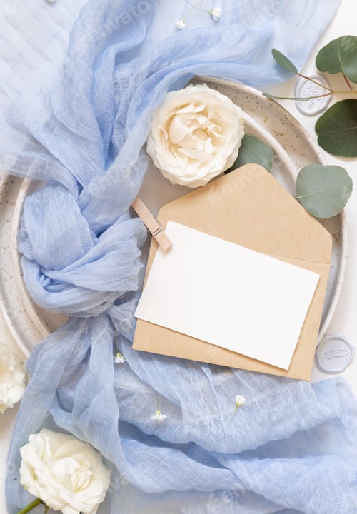 Preview: Card and envelope near blue tulle fabric and cream roses top view copy space, wedding mockup
