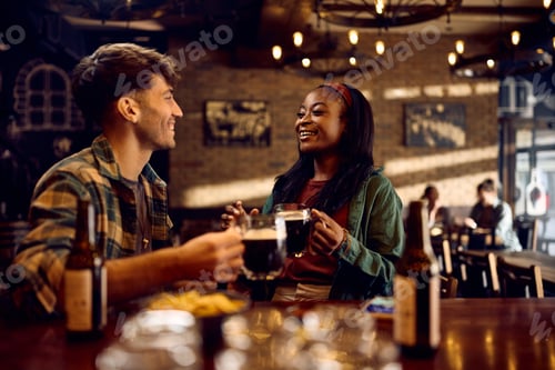 Preview: Happy black woman and her boyfriend talking while drinking beer in a bar.