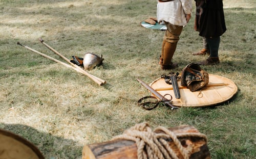 Preview: Medieval weapons on the grass. Round shield, swords, spears, helmet and legs of warriors outdoors