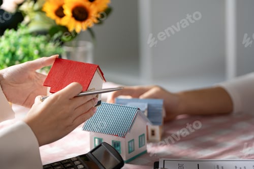 Preview: Hands Holding Model Houses with Calculator on Table - Real Estate Investment and Home Buying Concept