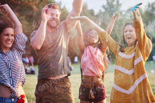 Preview: Four young adult friends dancing and throwing coloured chalk powder at Holi Festival