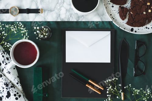 Preview: Top view of cup of tea next to white envelope on green backgroun