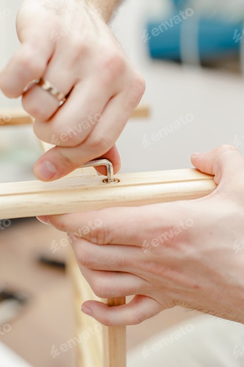 Preview: Male hands assemble wooden furniture by tightening the screw with a metal screwdriver