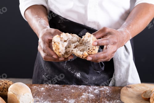 Preview: Midsection of african american male baker breaking baked bread over table