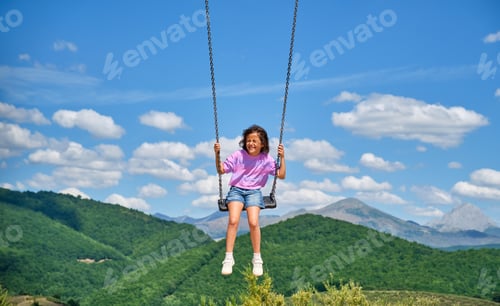 Preview: Little girl swinging on a very high swing with a mountain landscape in the background on a sunny day