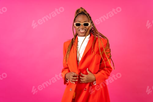 Preview: Black ethnic woman with braids on a pink background, portrait in a red suit and yellow pants smiling