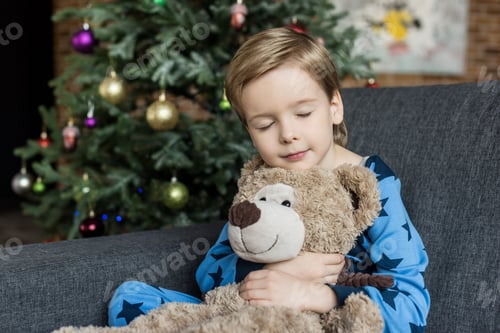 Preview: cute little child in pajamas hugging teddy bear while sleeping and sitting in sofa